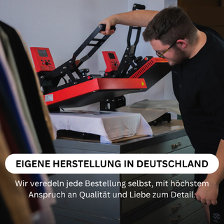 A man is operating a red and black industrial printing press in a workshop, with various printed materials visible on the press.