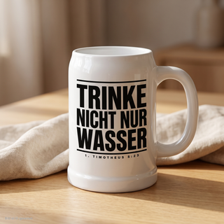 Weißer Bierkrug mit Bibelvers 1. Timotheus 5:23 auf einem Holztisch mit Leinentuch